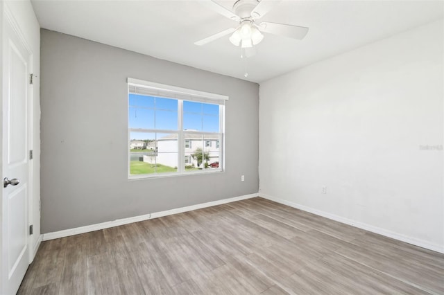 spare room with wood finished floors, a ceiling fan, and baseboards