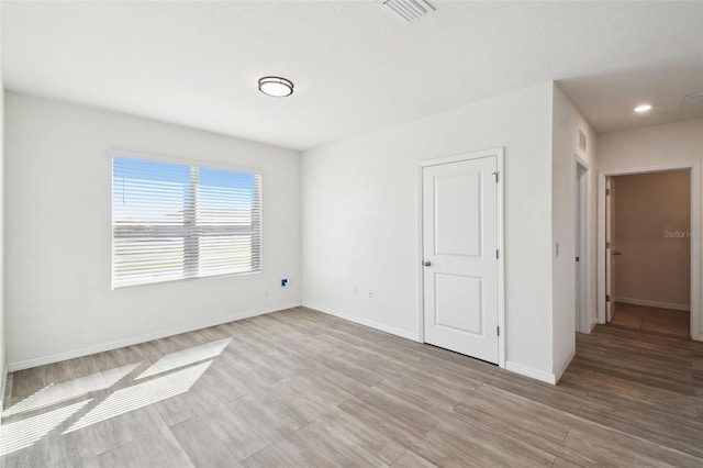 spare room featuring light wood-style flooring, visible vents, and baseboards