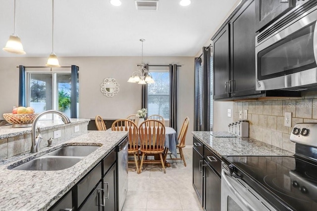 kitchen with visible vents, appliances with stainless steel finishes, light stone counters, hanging light fixtures, and a sink