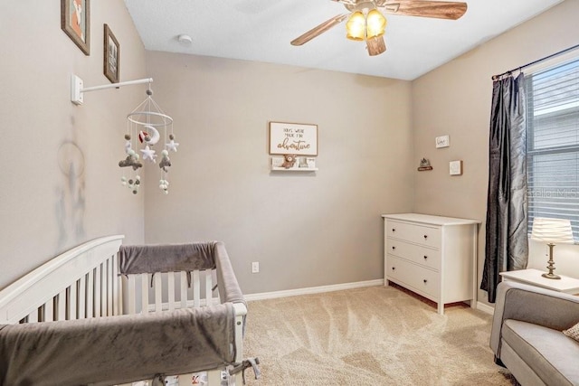 bedroom with light colored carpet, ceiling fan, a crib, and baseboards