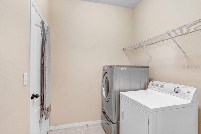 clothes washing area with washing machine and dryer, laundry area, baseboards, and light tile patterned floors