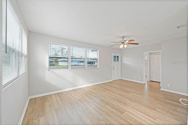 spare room featuring light wood-style floors, a healthy amount of sunlight, baseboards, and a ceiling fan