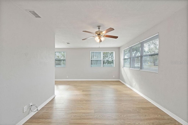 empty room with light wood-style floors, visible vents, baseboards, and a ceiling fan