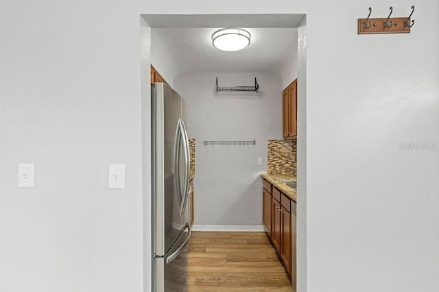 kitchen with light wood finished floors, decorative backsplash, freestanding refrigerator, and brown cabinets