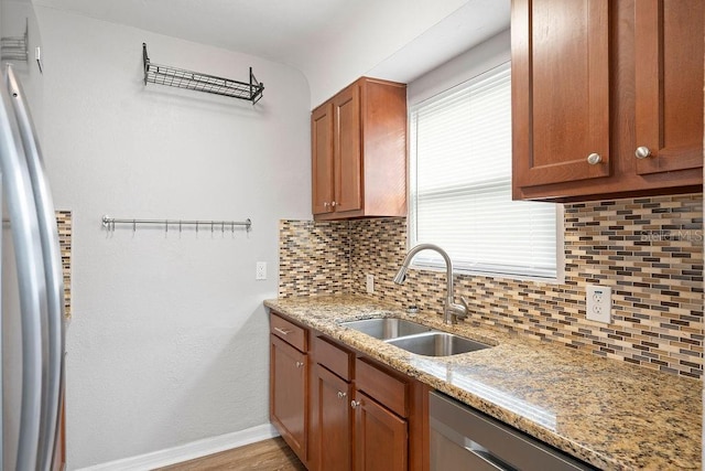 kitchen featuring light stone countertops, a sink, baseboards, stainless steel dishwasher, and decorative backsplash