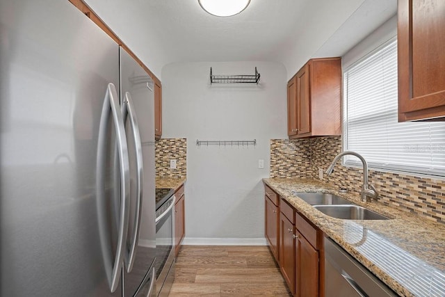 kitchen with stainless steel appliances, brown cabinetry, a sink, and light stone countertops