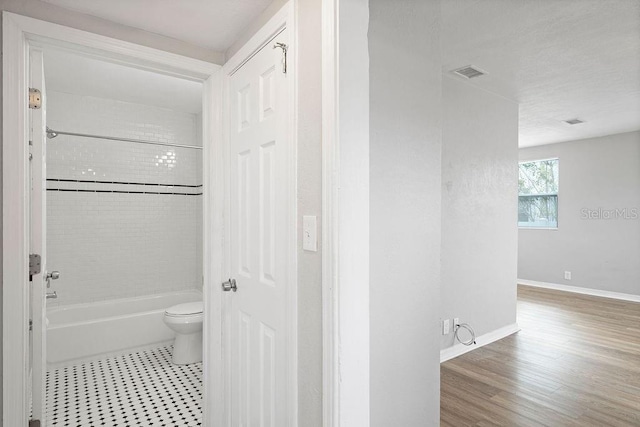 bathroom with baseboards, visible vents, toilet, wood finished floors, and shower / washtub combination