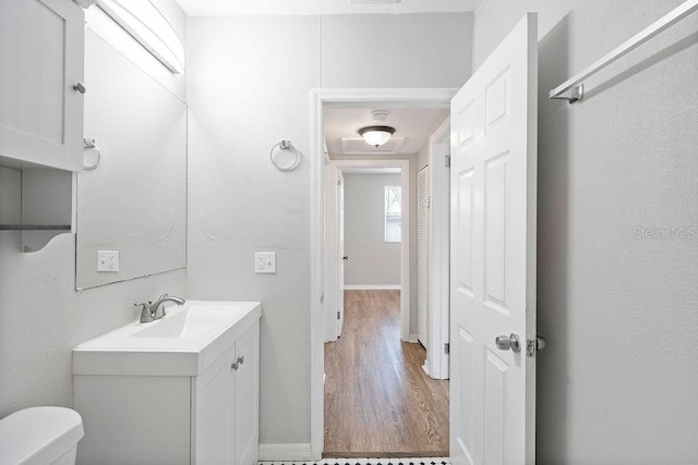 half bath with baseboards, vanity, toilet, and wood finished floors