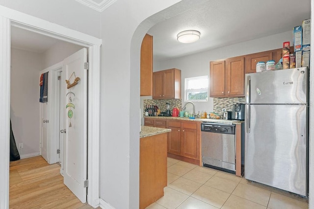 kitchen with tasteful backsplash, arched walkways, brown cabinetry, light stone countertops, and stainless steel appliances