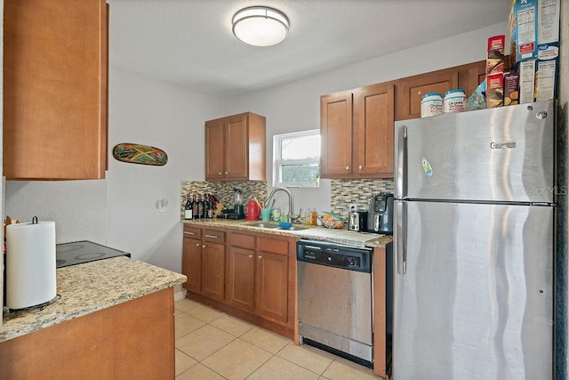 kitchen with light tile patterned flooring, a sink, appliances with stainless steel finishes, decorative backsplash, and brown cabinetry