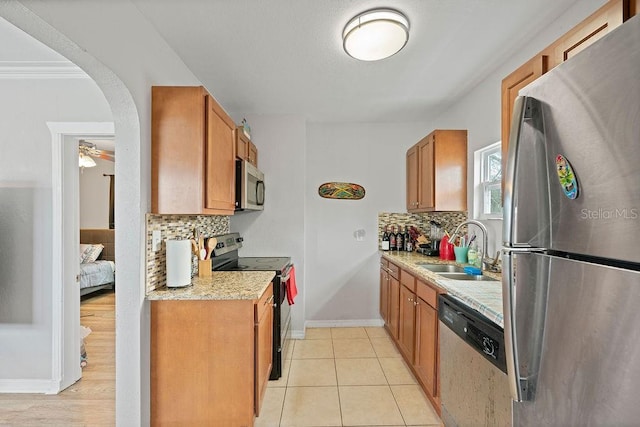 kitchen with arched walkways, stainless steel appliances, a sink, and brown cabinets