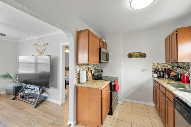 kitchen featuring arched walkways, appliances with stainless steel finishes, brown cabinetry, and a sink