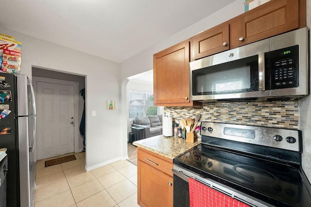 kitchen with light tile patterned floors, arched walkways, decorative backsplash, stainless steel appliances, and light countertops