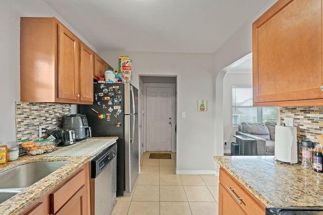 kitchen featuring light stone counters, decorative backsplash, appliances with stainless steel finishes, light tile patterned flooring, and baseboards