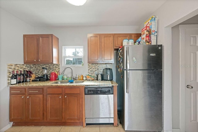 kitchen featuring light stone counters, a sink, appliances with stainless steel finishes, backsplash, and brown cabinets