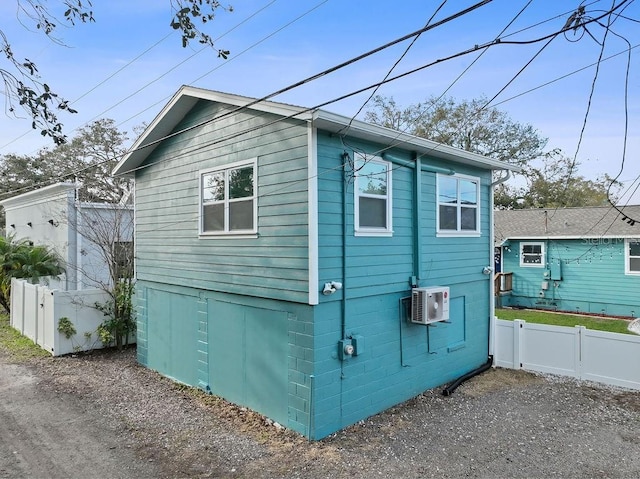 view of home's exterior with a wall unit AC, driveway, and fence