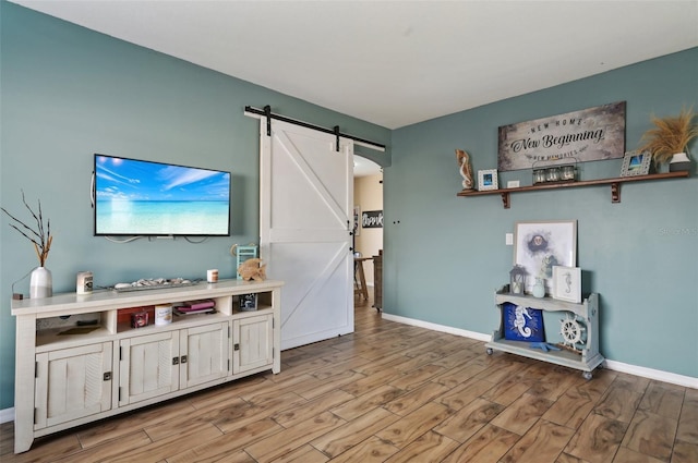 living room featuring a barn door, light wood-type flooring, and baseboards