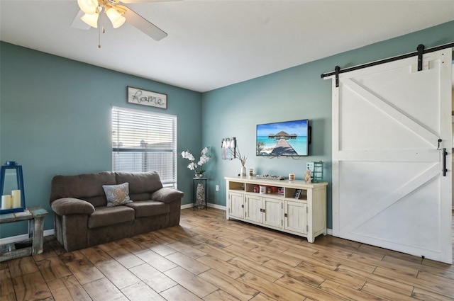 living area featuring light wood-style floors, a barn door, baseboards, and ceiling fan