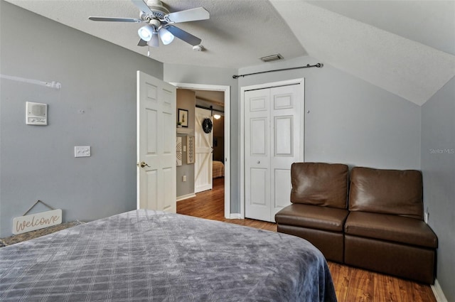 bedroom featuring lofted ceiling, a closet, visible vents, a textured ceiling, and wood finished floors