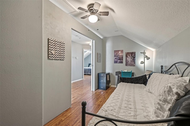 bedroom with a textured ceiling, a textured wall, wood finished floors, baseboards, and vaulted ceiling