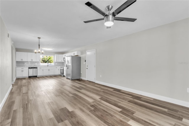 unfurnished living room featuring ceiling fan with notable chandelier, light wood-type flooring, a sink, and baseboards