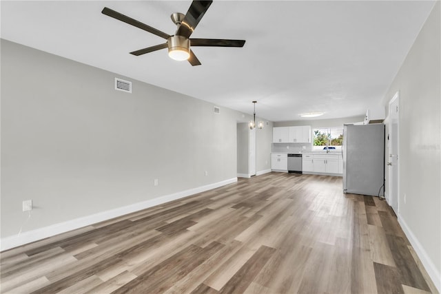 unfurnished living room featuring light wood-style floors, baseboards, visible vents, and ceiling fan with notable chandelier