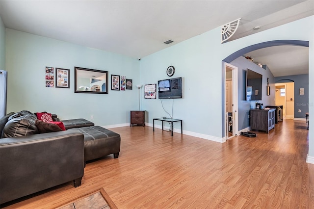 living area with arched walkways, baseboards, visible vents, and wood finished floors