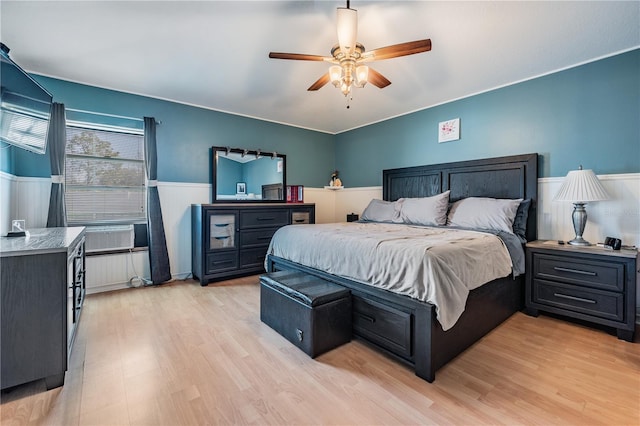 bedroom with a ceiling fan, wainscoting, light wood-style flooring, and cooling unit