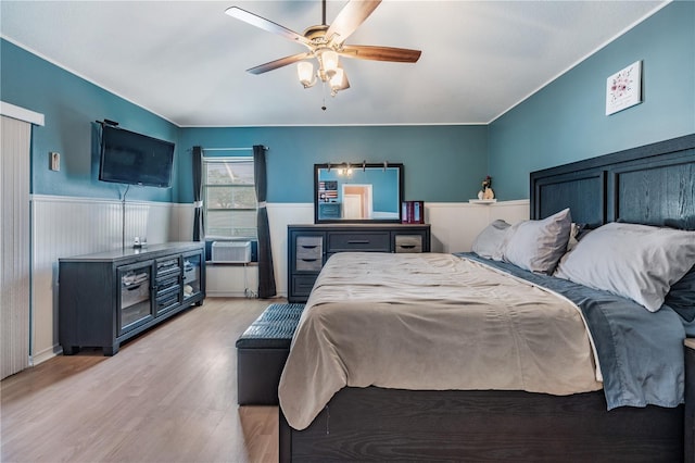 bedroom with cooling unit, light wood-style floors, a ceiling fan, and a wainscoted wall