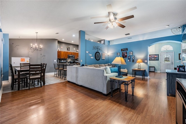 living area featuring baseboards, vaulted ceiling, ceiling fan with notable chandelier, and light wood-type flooring