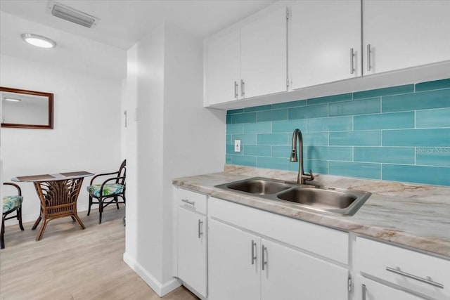 kitchen featuring light wood finished floors, visible vents, light countertops, white cabinetry, and a sink