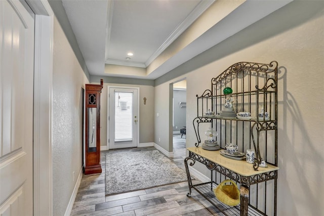 entryway with a textured wall, wood finished floors, baseboards, ornamental molding, and a raised ceiling