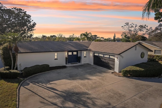 ranch-style house with concrete driveway, roof with shingles, an attached garage, and stucco siding