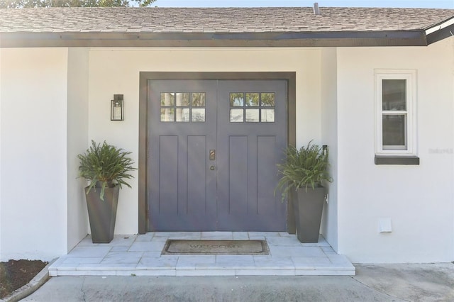 entrance to property featuring a shingled roof and stucco siding