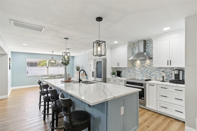 kitchen with white cabinetry, wall chimney exhaust hood, a kitchen island with sink, and appliances with stainless steel finishes