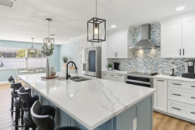 kitchen featuring wall chimney exhaust hood, a center island with sink, stainless steel appliances, and a sink