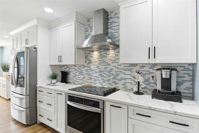 kitchen featuring light stone counters, stainless steel appliances, white cabinetry, wall chimney range hood, and light wood-type flooring