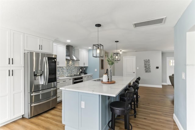 kitchen with stainless steel appliances, visible vents, white cabinets, a large island, and wall chimney exhaust hood