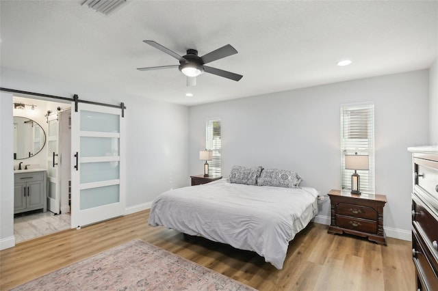 bedroom with light wood finished floors, visible vents, a barn door, a sink, and baseboards