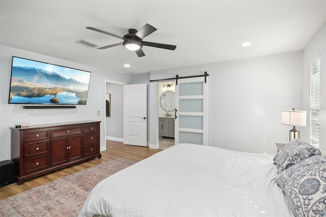 bedroom featuring light wood finished floors, a barn door, visible vents, connected bathroom, and recessed lighting