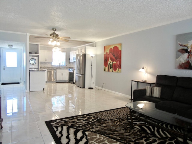 living area with a textured ceiling, a ceiling fan, baseboards, washer / clothes dryer, and crown molding