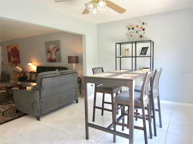 dining room featuring light tile patterned floors, a ceiling fan, baseboards, and a textured ceiling