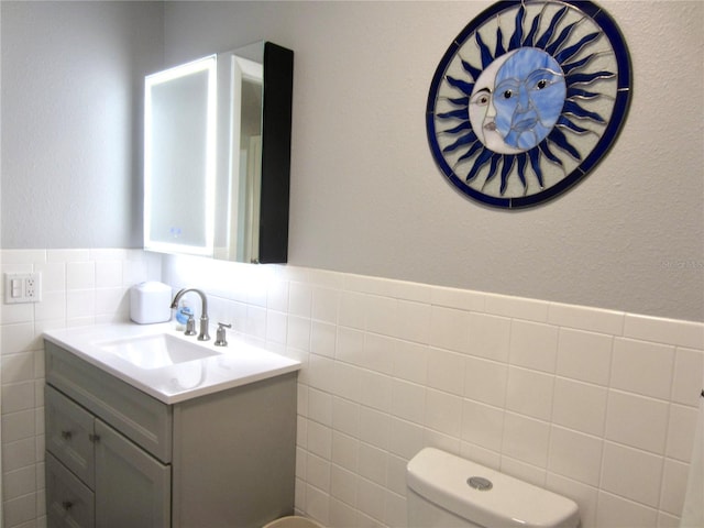 half bath with tile walls, a wainscoted wall, vanity, and toilet