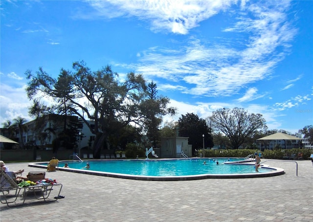 community pool with a patio area, a shed, fence, and an outdoor structure