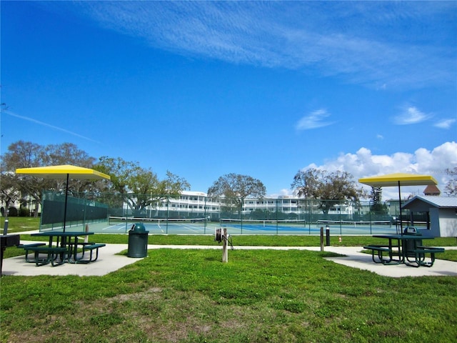 view of community featuring a tennis court, a yard, and fence