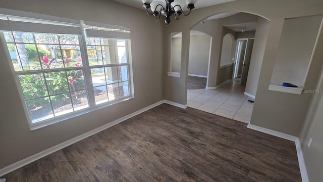 unfurnished dining area featuring baseboards, arched walkways, dark wood-type flooring, and a notable chandelier