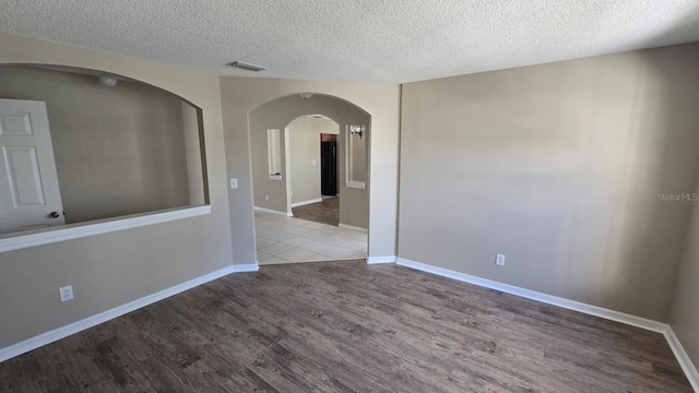 empty room with a textured ceiling, arched walkways, light wood-style flooring, visible vents, and baseboards