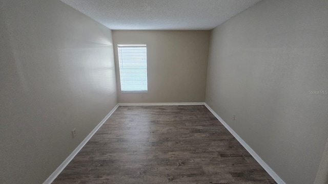 empty room with dark wood-style floors, a textured ceiling, and baseboards