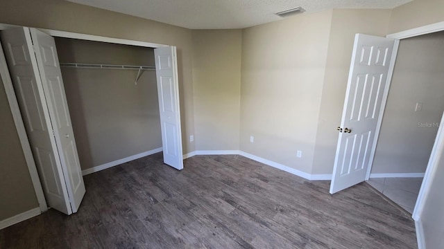 unfurnished bedroom featuring dark wood-style floors, baseboards, visible vents, and a closet