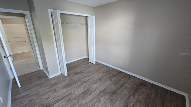 unfurnished bedroom featuring dark wood-style flooring, a closet, and baseboards